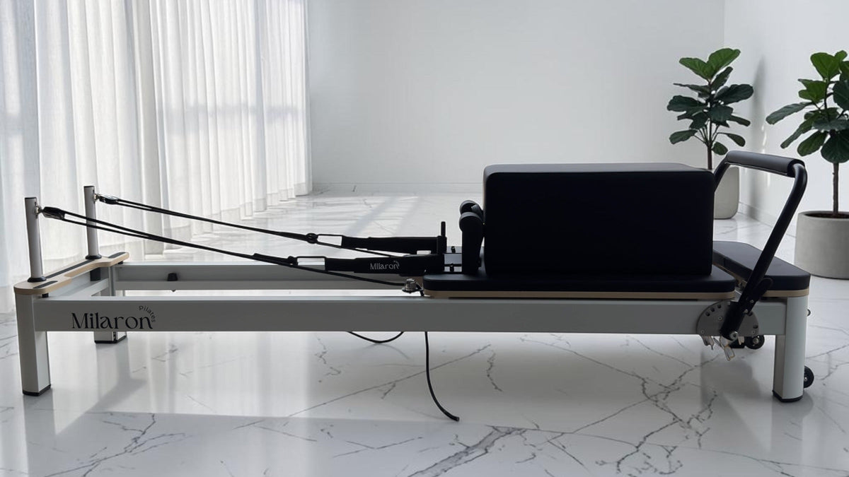 A Pearl Studio reformer on a white marble floor in a bright room with sheer curtains and two plants