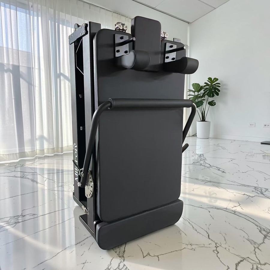Milaron Pearl Foldable reformer folded upright for storage, black upholstery on a 6063-T5 aluminium frame.