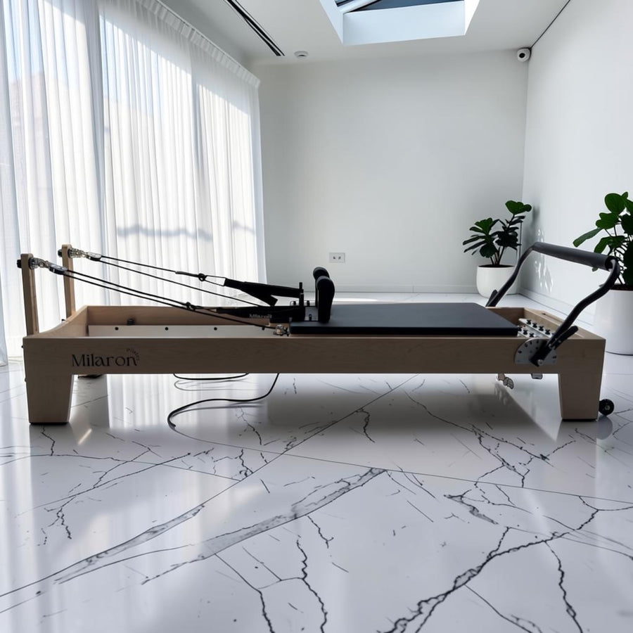 Milaron Maple Studio reformer with a maple wood frame and black upholstery, set up in a sunlit room with marble floors.